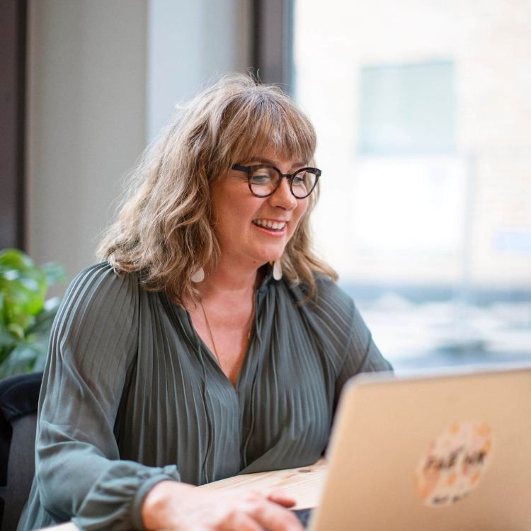 Smiling woman with glasses working on a laptop in a bright room